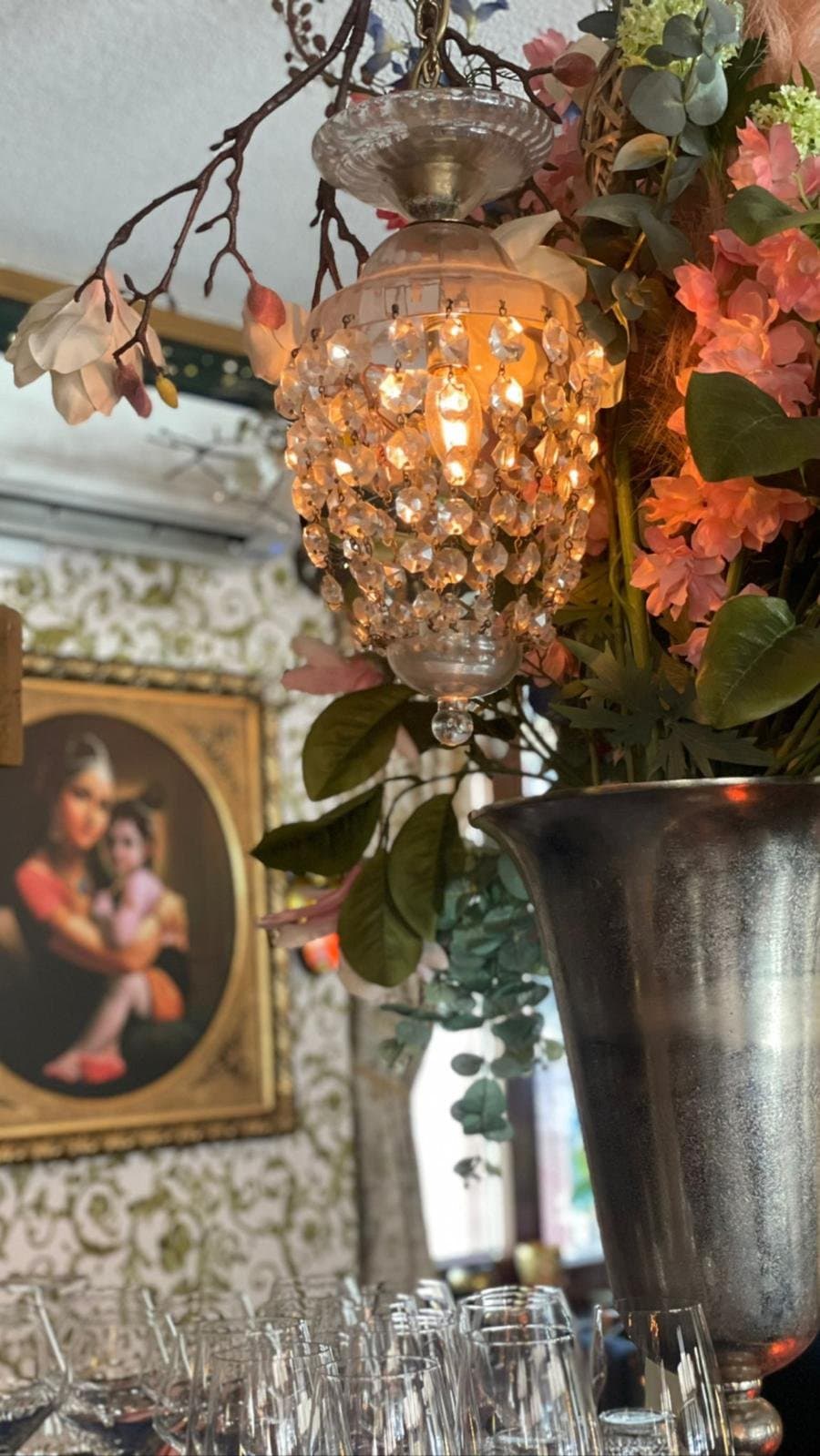 A crystal lamp among flowers, with a framed painting on the wall behind.