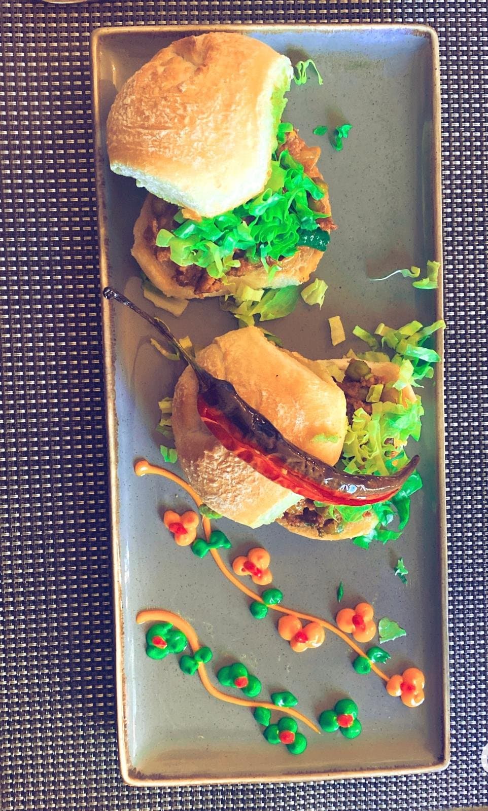 Two small spiced buns with a roasted red chilli on a grey plate.