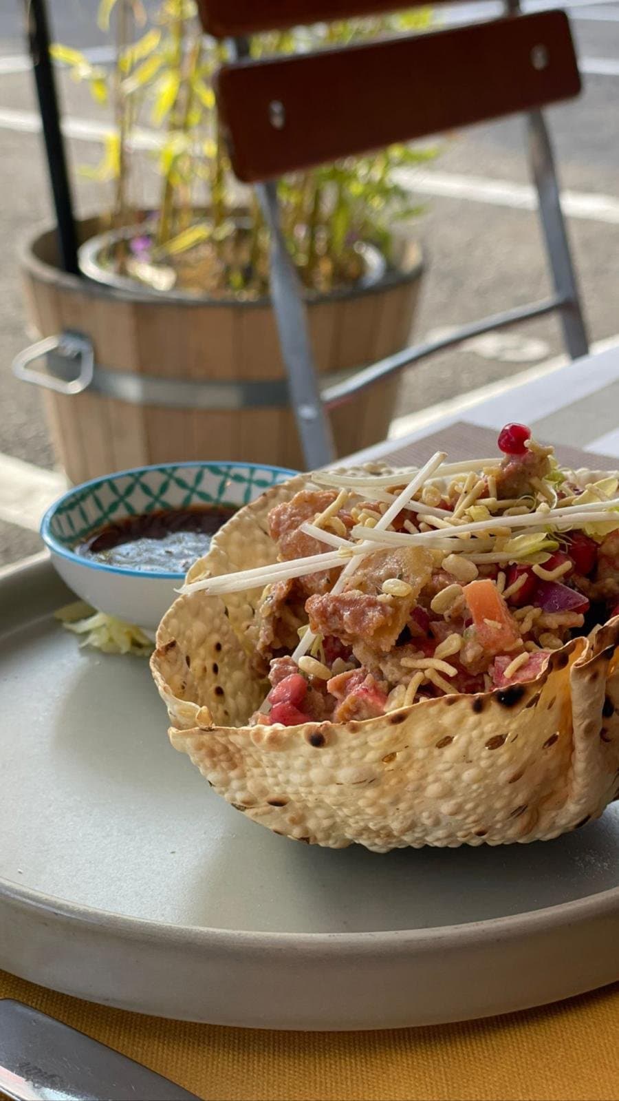 A filled poppadum basket with a dipping sauce, on a terrace table.