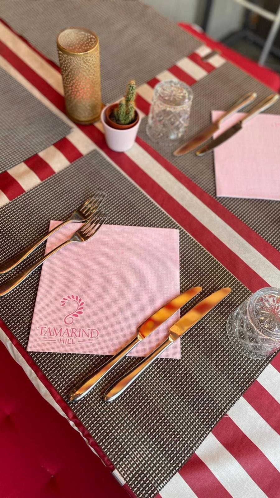 A table laid for two with the Tamarind Hill napkin, cutlery and a golden candle holder.